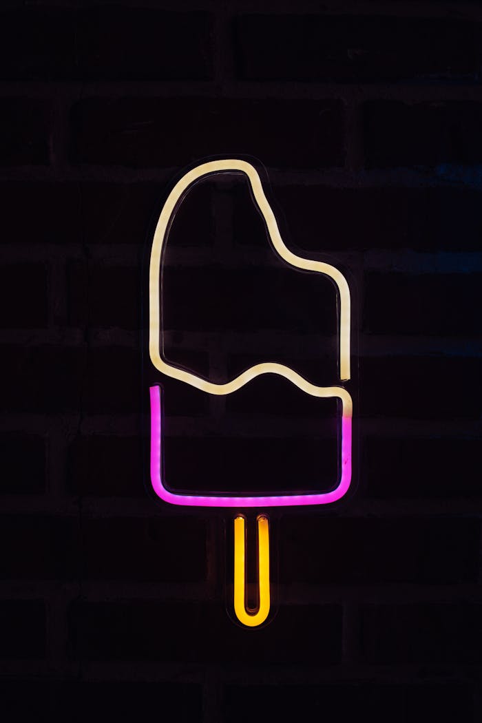 Vibrant neon ice cream sign glowing against a dark brick background, creating a modern and playful vibe.